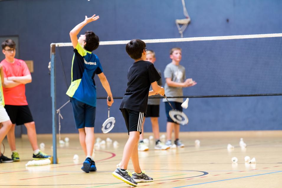 Gruppe von Kindern beim Badmintontraining in einer Sporthalle, mit Schlägern und Federbällen auf dem Boden.
