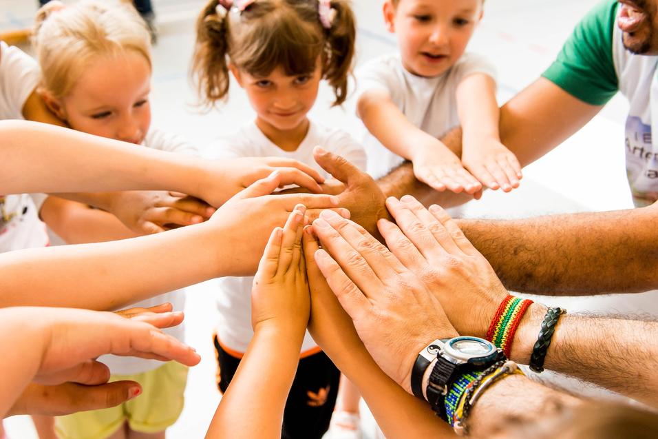 Kinder und Erwachsene legen ihre Hände in einem Kreis zusammen, symbolisieren Zusammenarbeit und Gemeinschaft.